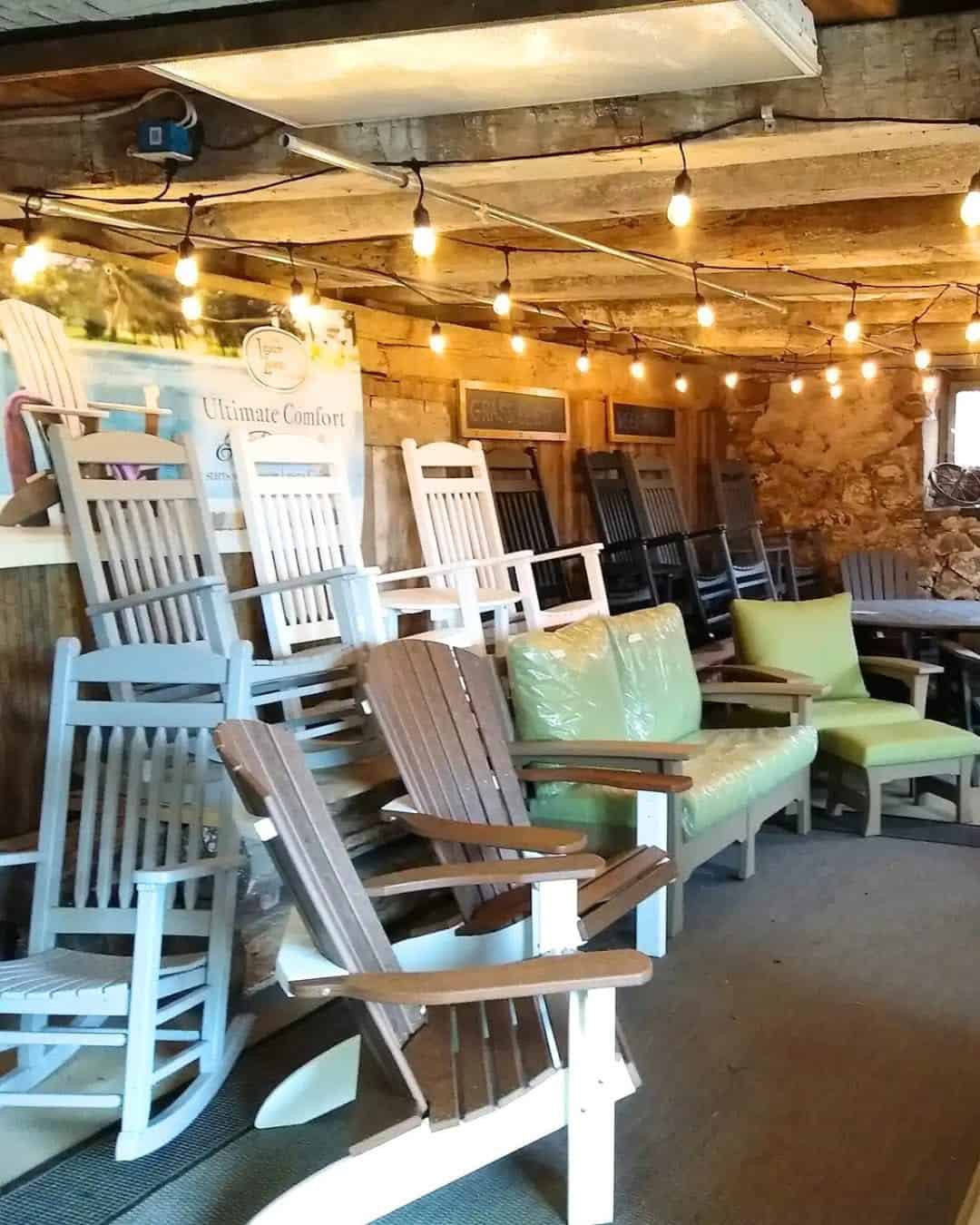 Indoor furniture showroom displaying rows of wooden rocking chairs under string lights, with a rustic brick wall backdrop.