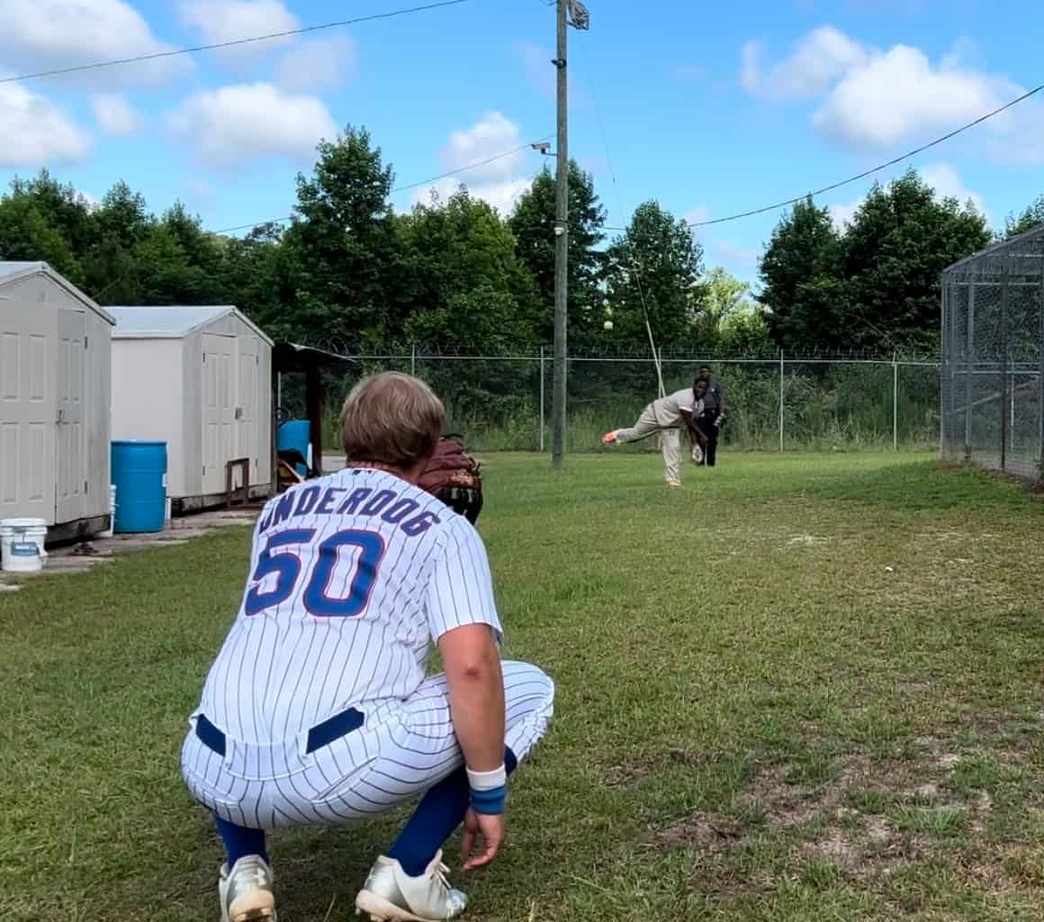 Underdog baseball player crouching with glove, ready to catch, in a grassy field during a game.