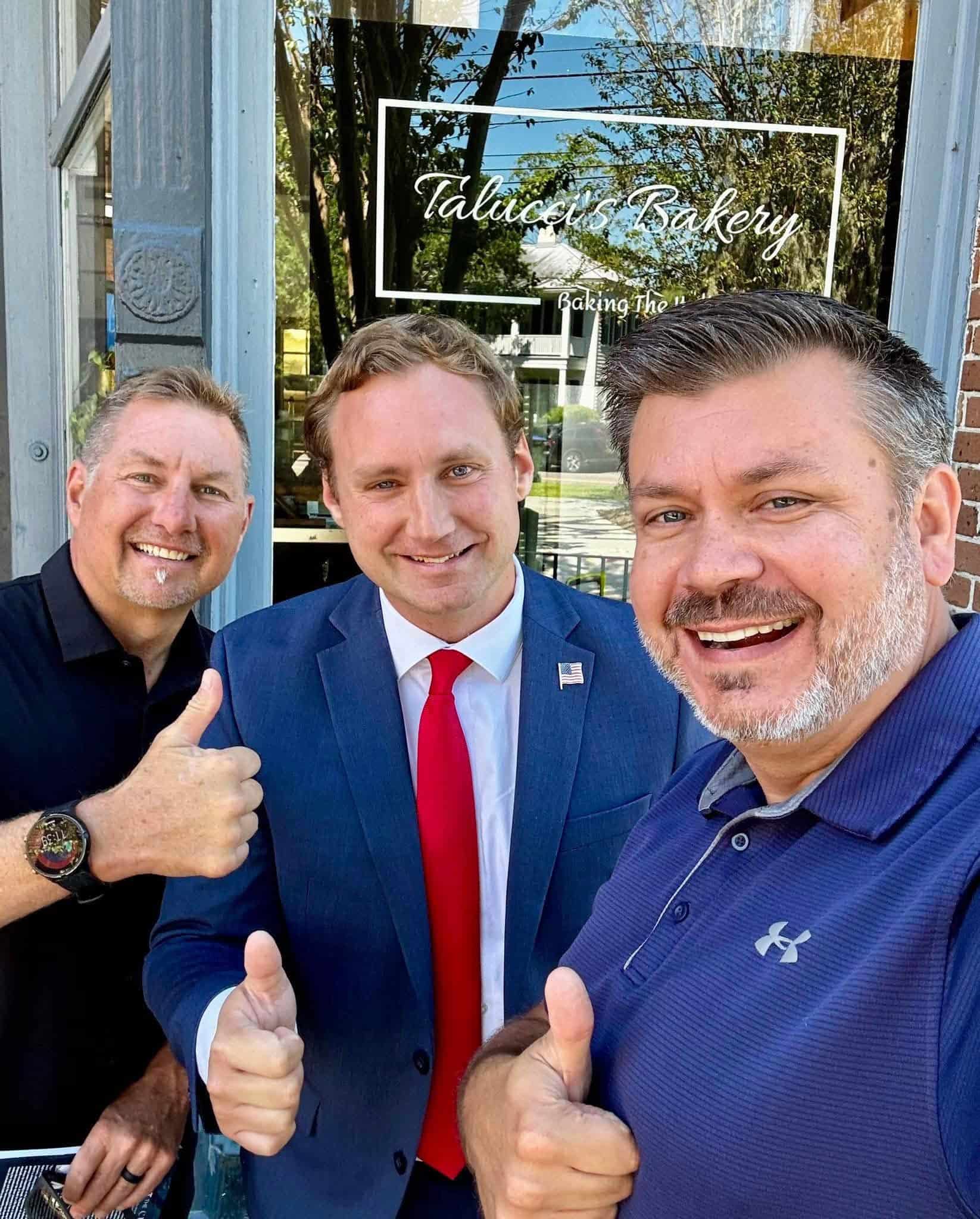 Three men smiling and giving thumbs up in front of a bakery window with Talice's Bakery sign.