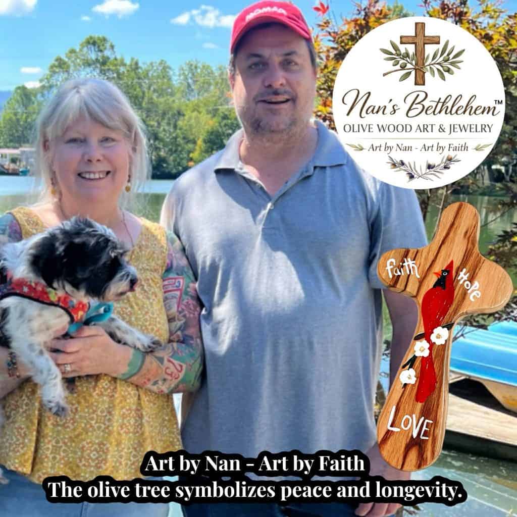 Two people smiling outdoors with a small dog; on the right is a round logo for Nan's Bethlehem Olive Wood Art & Jewelry featuring a cross and olive branches.