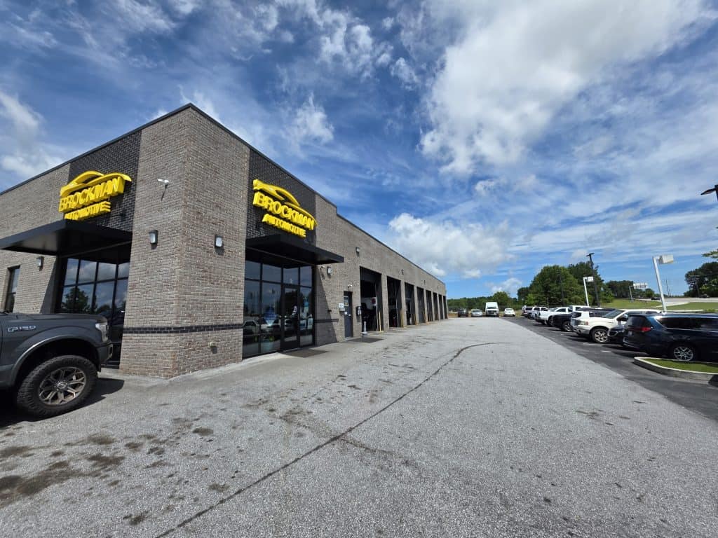 Brockman Automotive storefront with a yellow logo on a brick building under a blue sky.