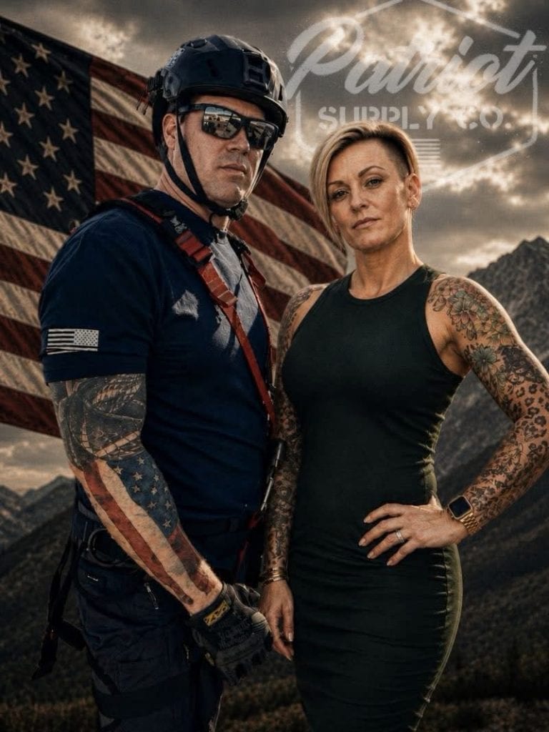Man in tactical gear and helmet with sunglasses stands beside a tattooed woman in a sleeveless black dress; a large American flag and rugged mountains are in the background, with a faint brand logo overhead.
