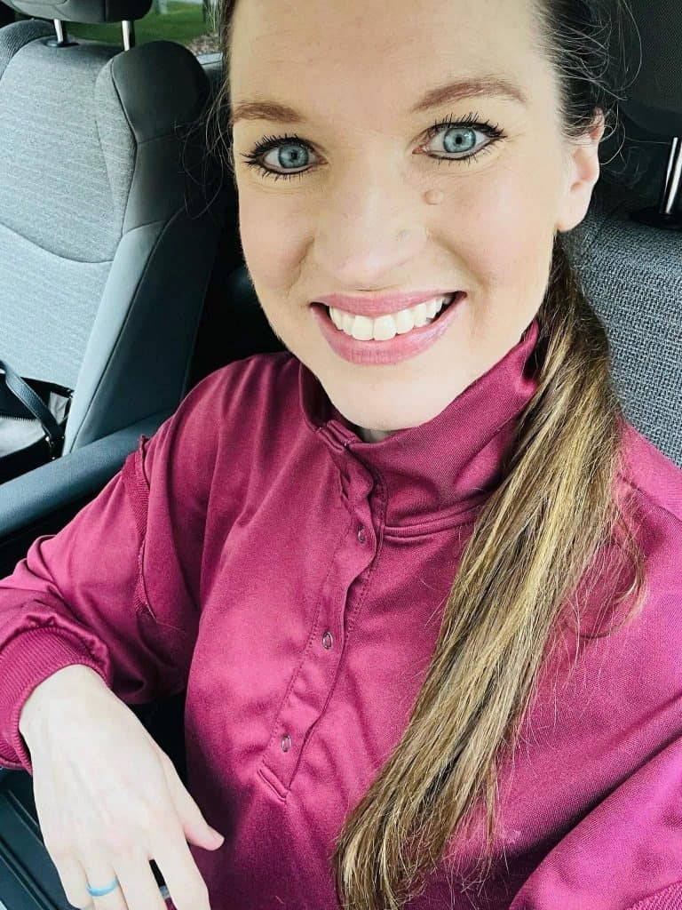 Close-up of a smiling woman in a car wearing a maroon blouse, long hair over her shoulder.