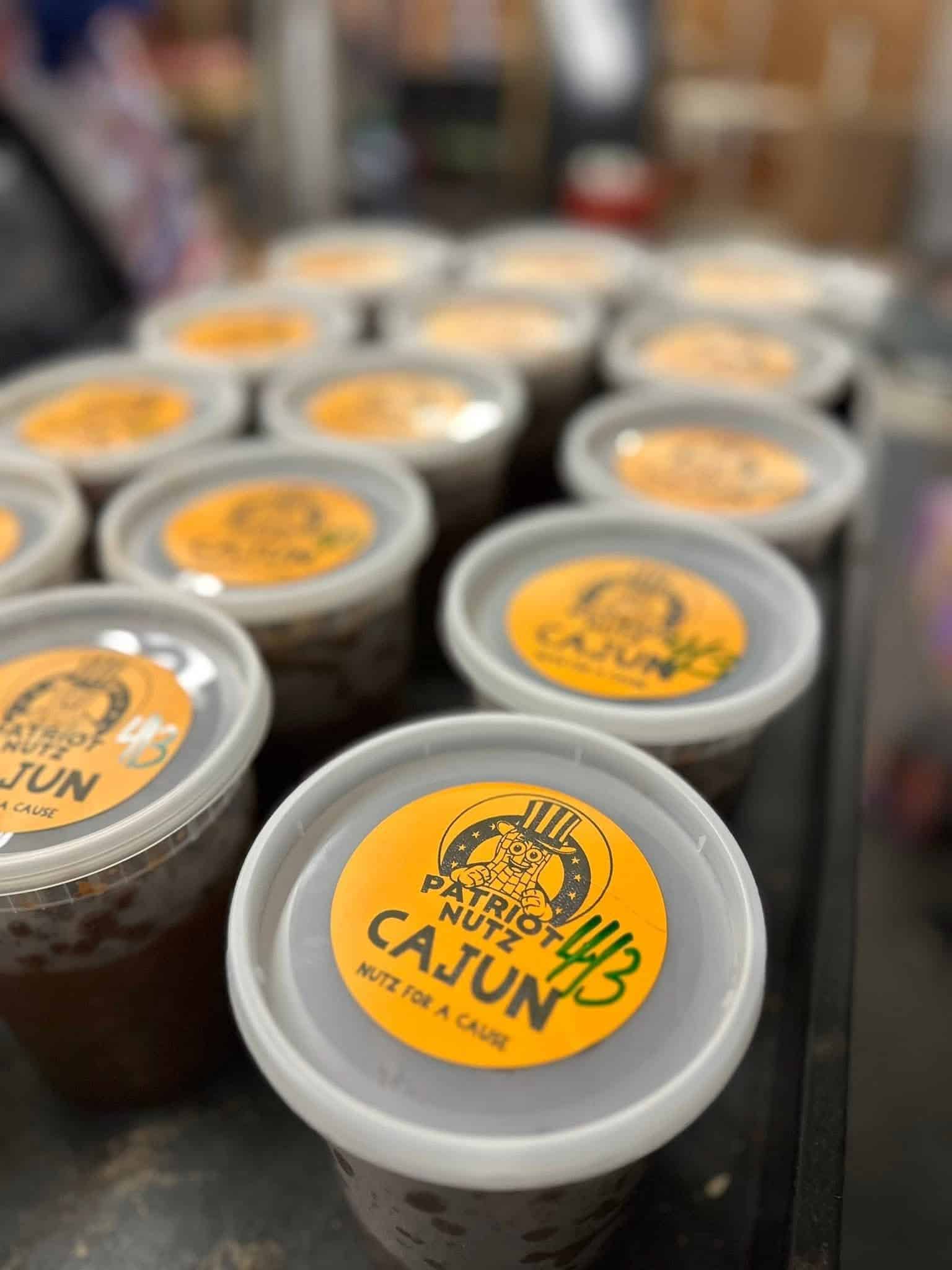 Row of takeout cups with grey lids and orange circular labels in a storefront or display case, out of focus in the background.