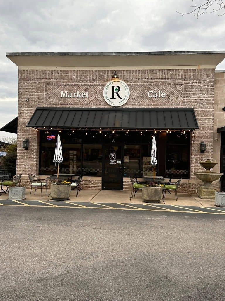 Cafe storefront with a brick exterior, black awning, and outdoor seating under umbrellas in front of a Market Café sign.
