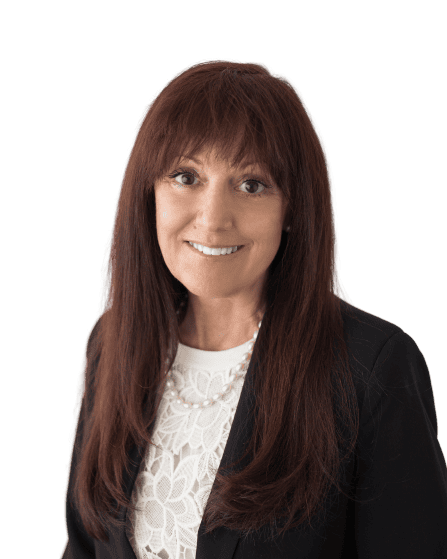 Professional headshot of a smiling woman with long brown hair, wearing a white lace blouse, pearl necklace, and black blazer.